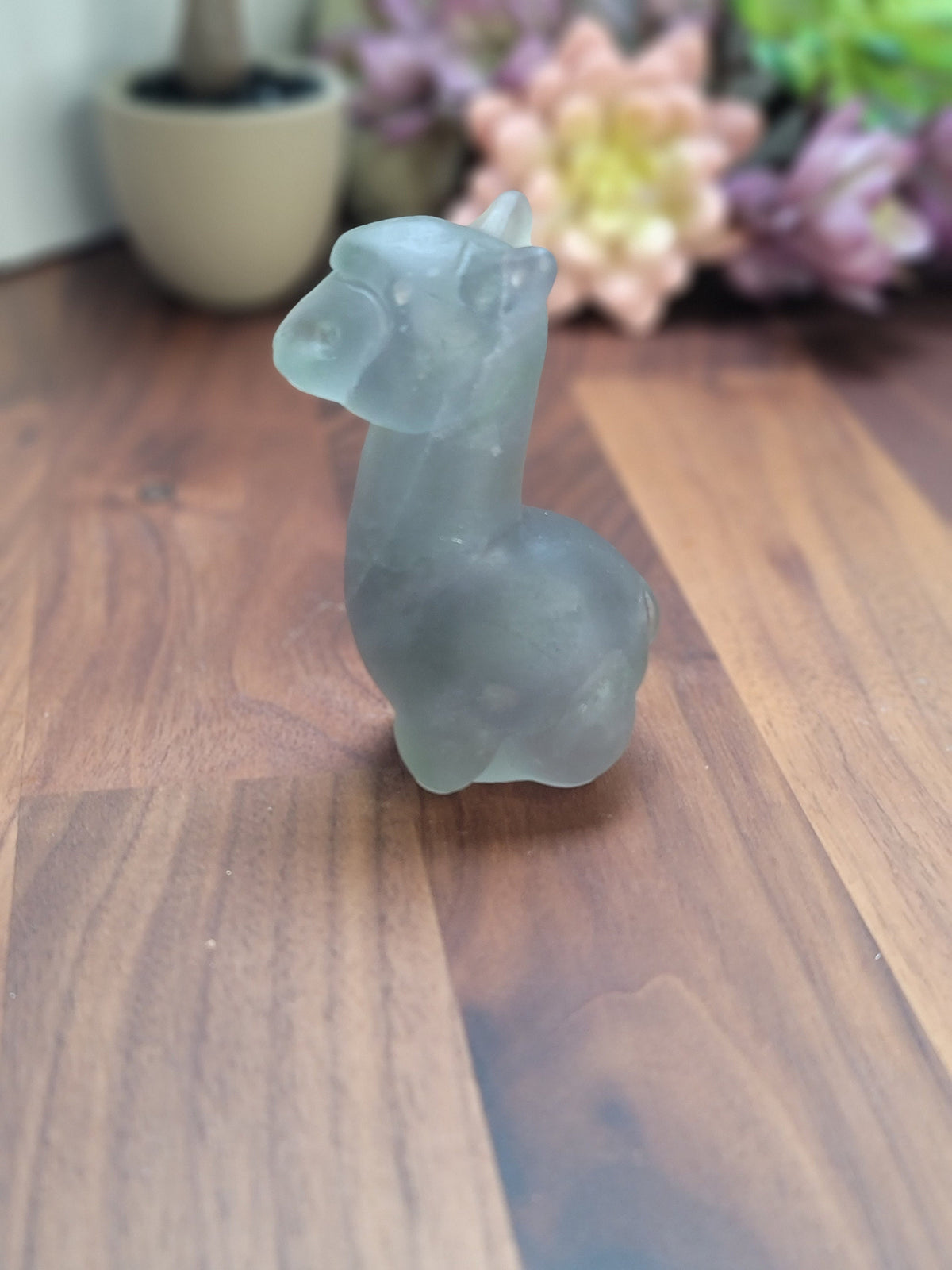 May include: A frosted glass llama figurine. The llama is standing on a wooden surface.