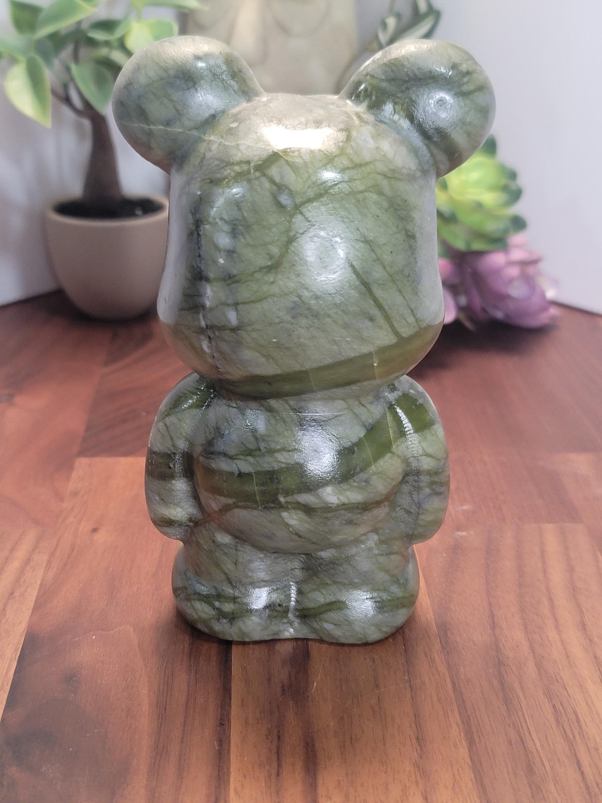 a green and white stone figurine of a bear sitting on a wooden surface.
