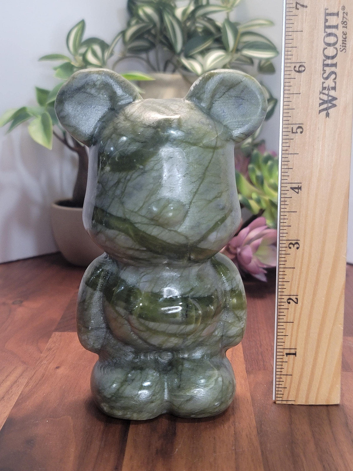 A green marble bear figurine is sitting on a wooden surface, with a ruler placed next to it to indicate its size.