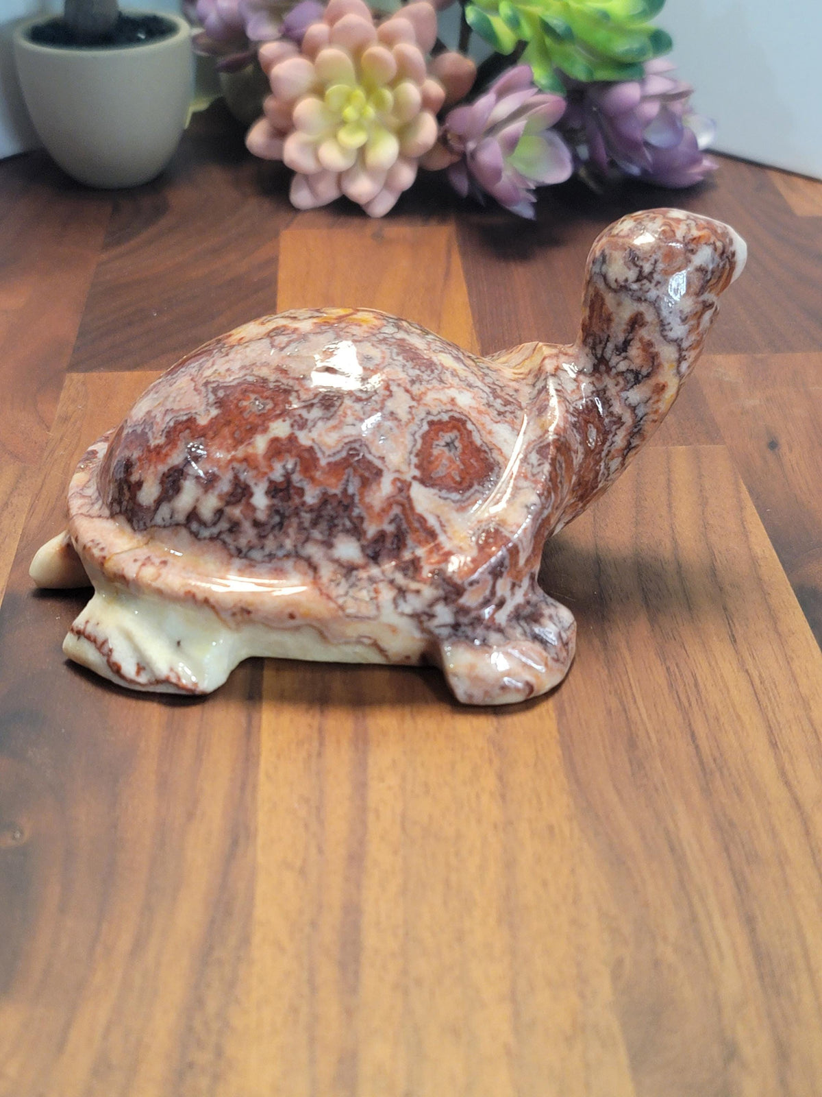 A ceramic turtle figurine is sitting on a wooden surface, with a vase of flowers in the background.