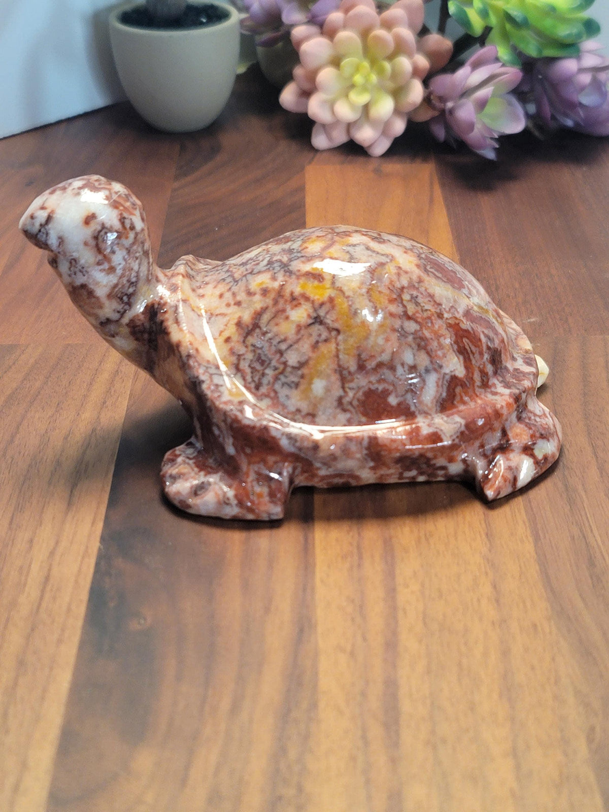 A ceramic turtle figurine is sitting on a wooden surface, with a bouquet of colorful flowers in the background.