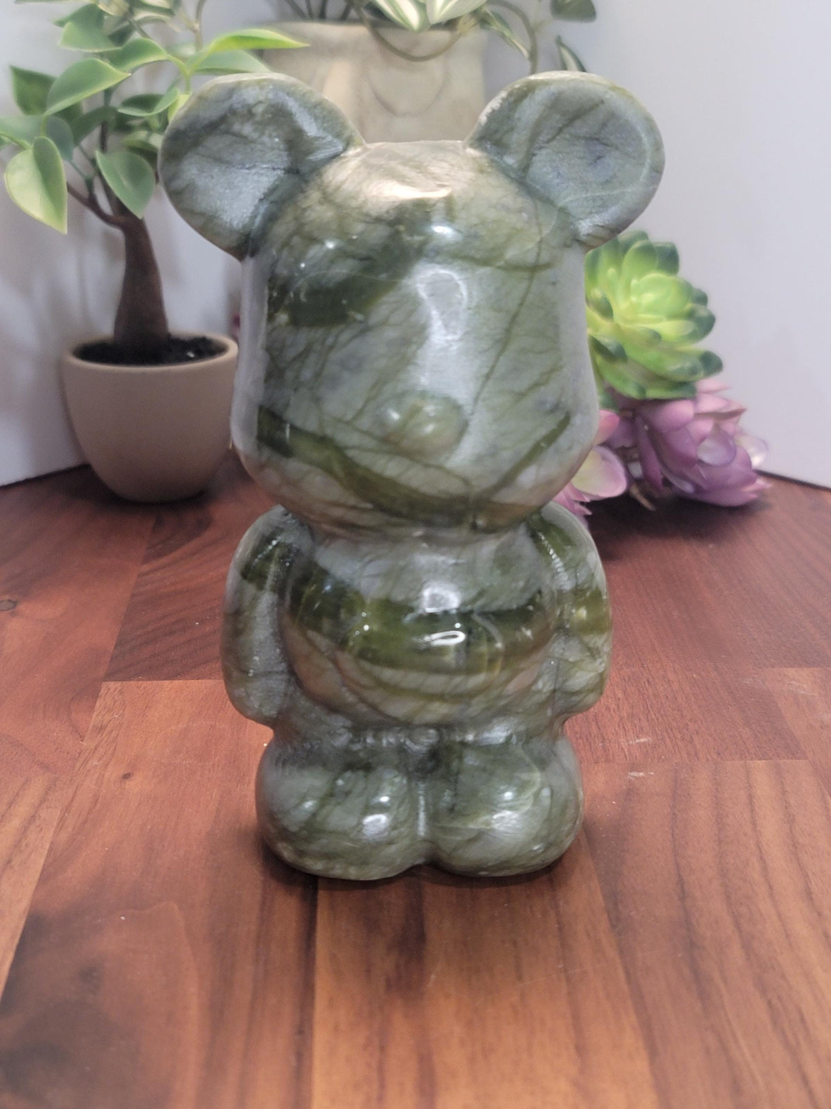 a green stone bear figurine sitting on a wooden surface.