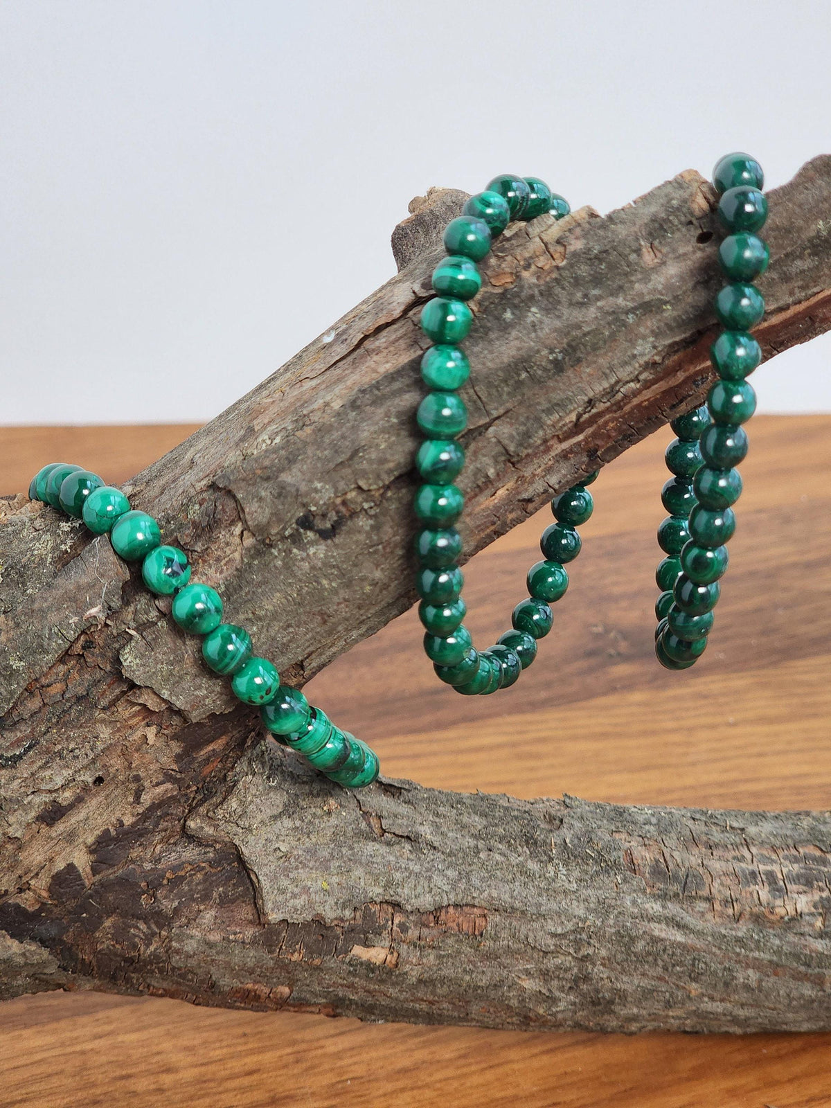 a collection of green beads, possibly malachite, arranged on a wooden surface. The beads are hanging from a branch or a piece of driftwood, creating a rustic and natural display.