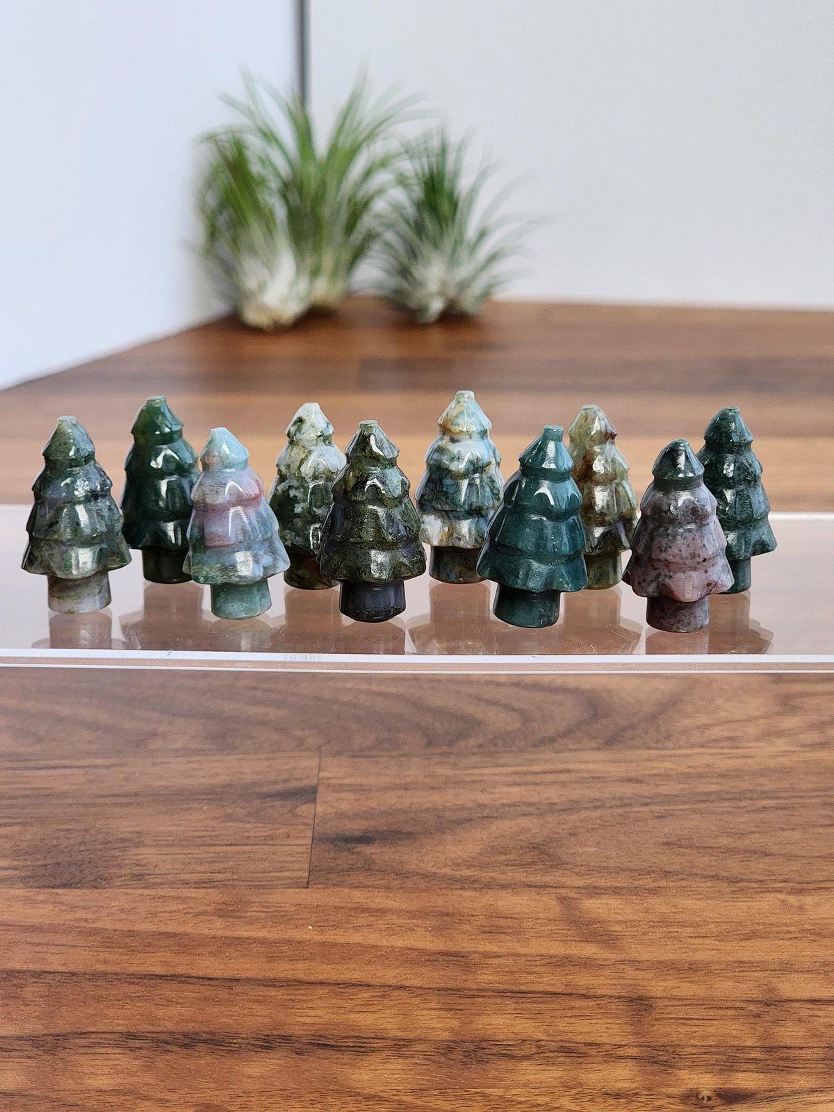 A collection of small, colorful tree-shaped figurines is displayed on a wooden surface, with a plant in the background.
