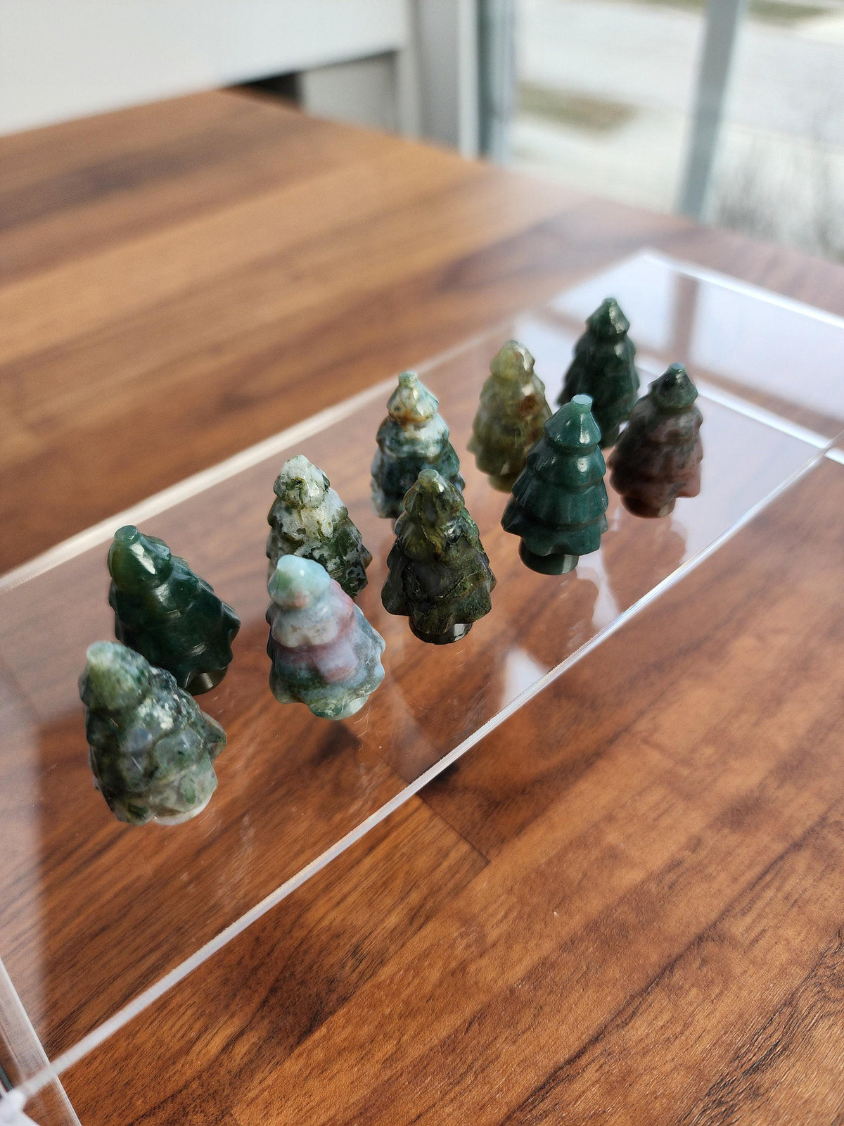 A collection of small, green jade figurines arranged on a clear glass surface, resembling miniature trees.