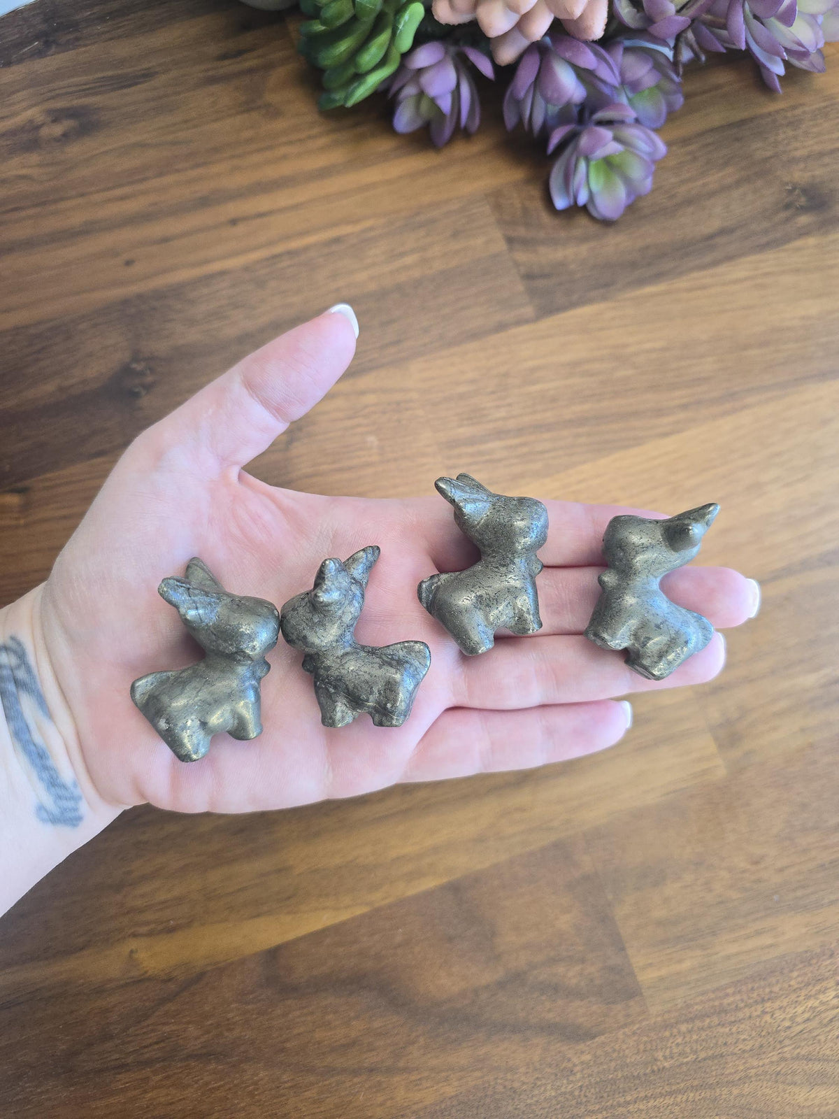 A hand holding four small, silver-colored metal figurines against a wooden background.