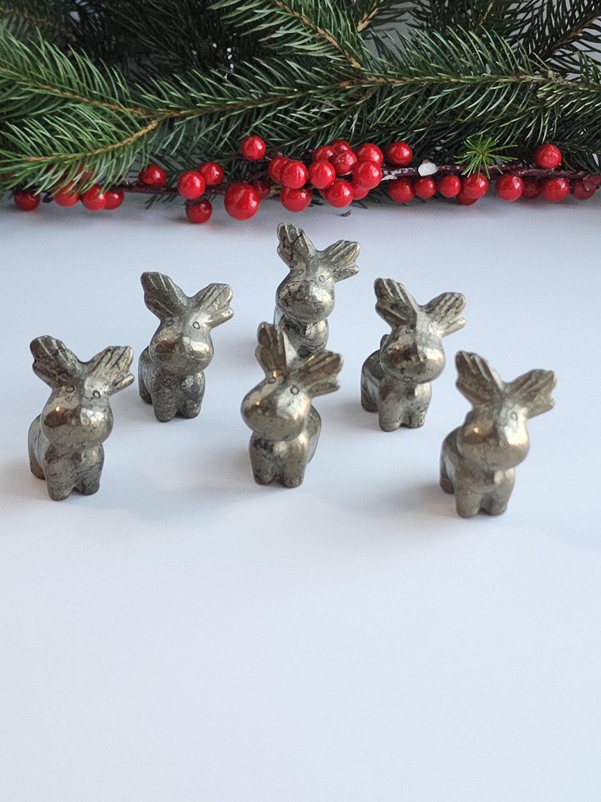 six silver-colored metal figurines of reindeer or deer-like animals, arranged in a circular pattern on a white background.