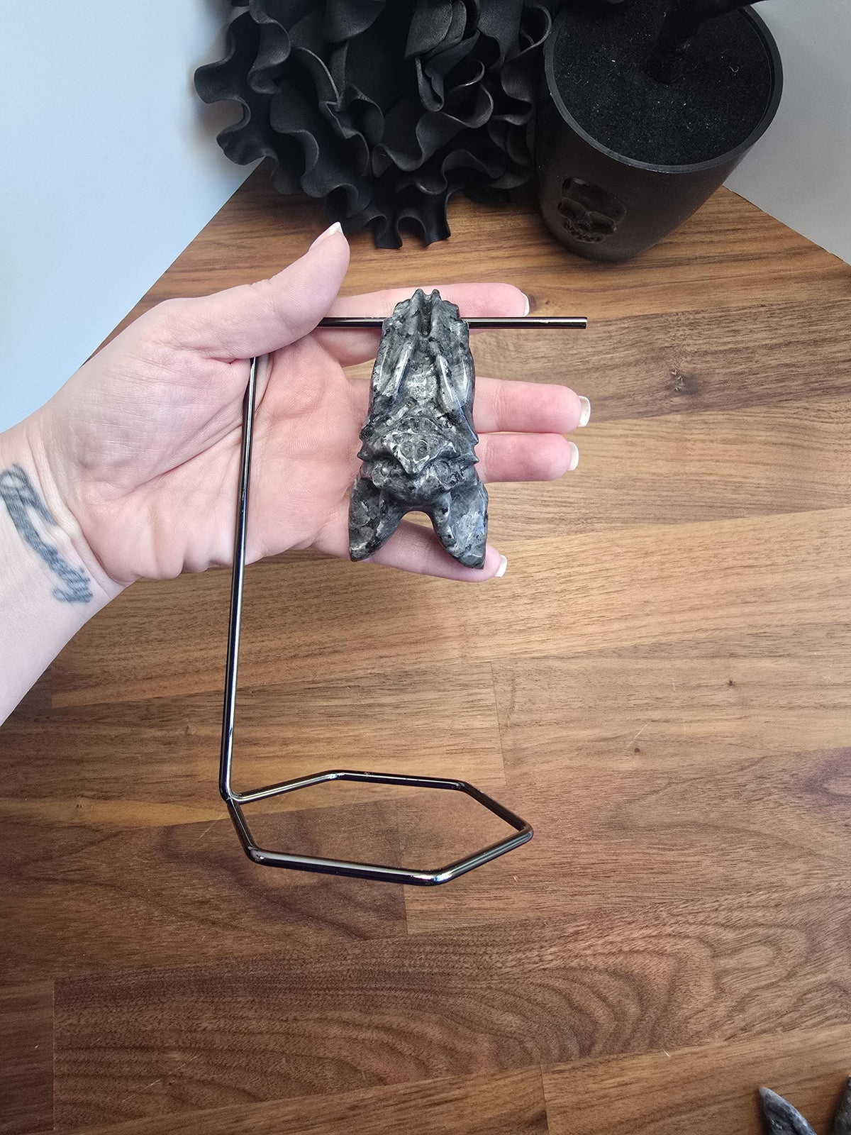 A hand is holding a small, black, metal object resembling a bat or a similar creature, which is mounted on a metal stand or holder.