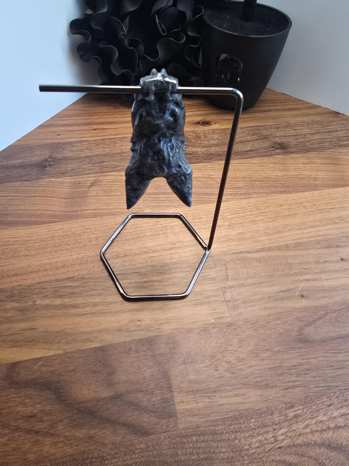 a unique, handcrafted bat sculpture hanging from a metal stand on a wooden surface.