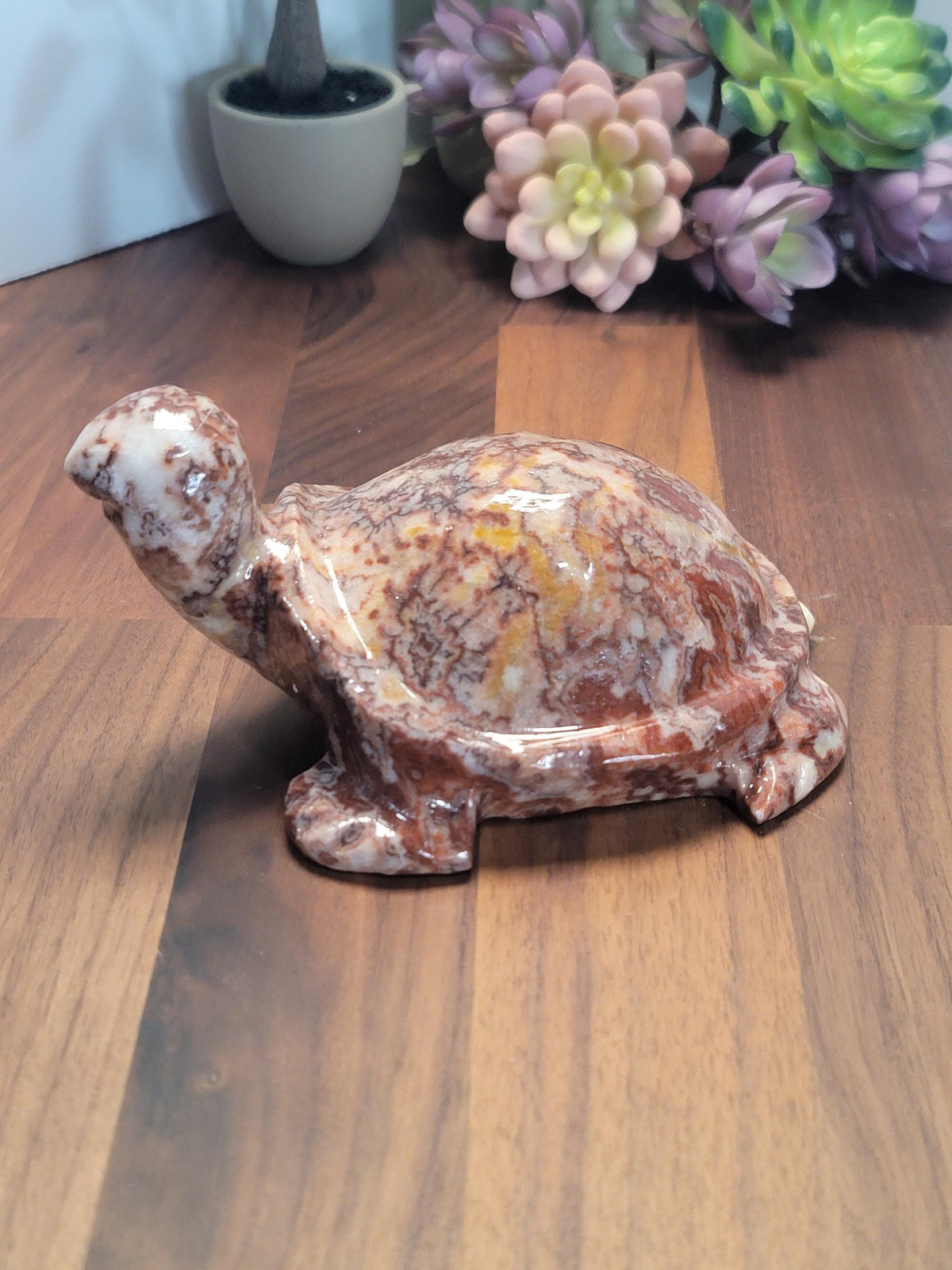A marble turtle figurine is sitting on a wooden surface, with a vase of colorful flowers in the background.