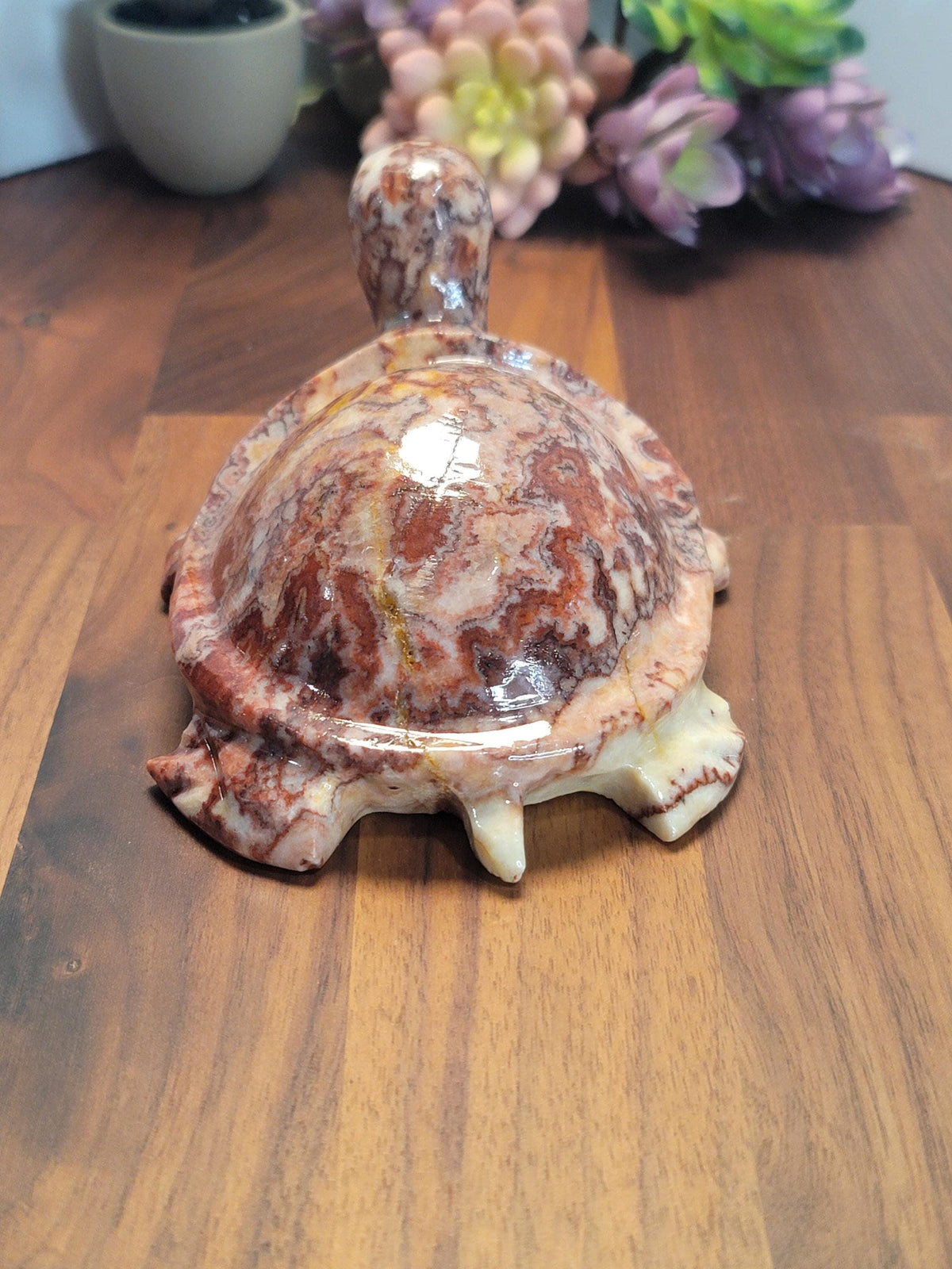 A ceramic turtle figurine with a marbled pattern sits on a wooden surface, with a bouquet of flowers in the background.