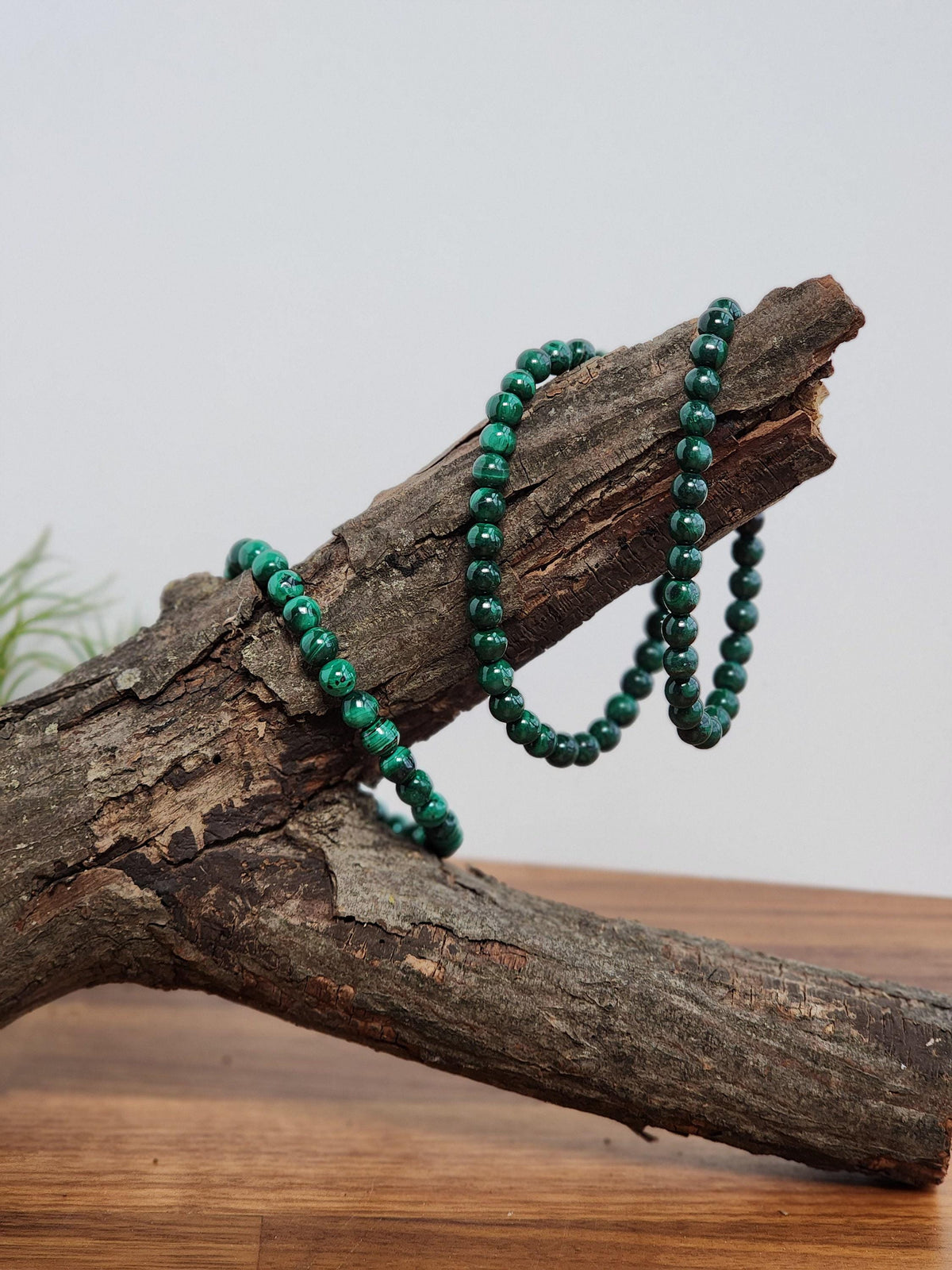 A pair of green beads is resting on a wooden log, creating a rustic and natural aesthetic.
