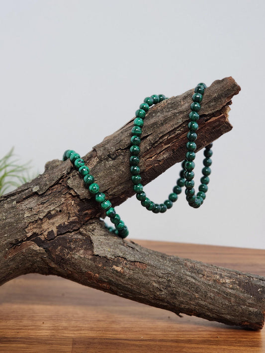 A pair of green beads is resting on a wooden log, creating a rustic and natural aesthetic.