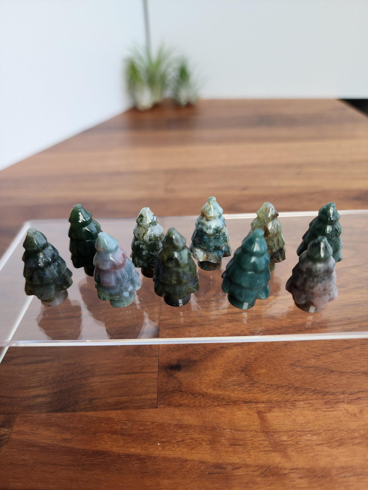 A collection of small, colorful jade figurines arranged on a clear display stand, with a blurred background suggesting a natural setting.