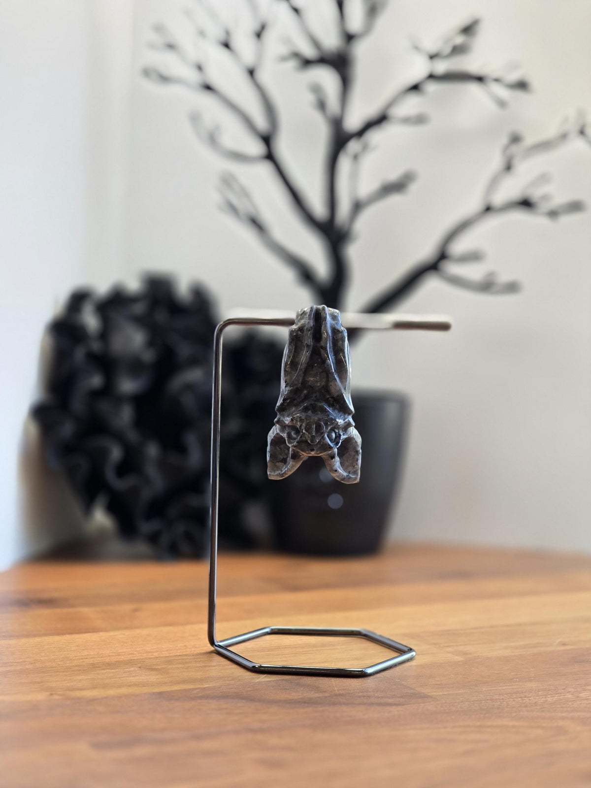 A small metal sculpture of a bat is displayed on a stand, with a black tree branch in the background.