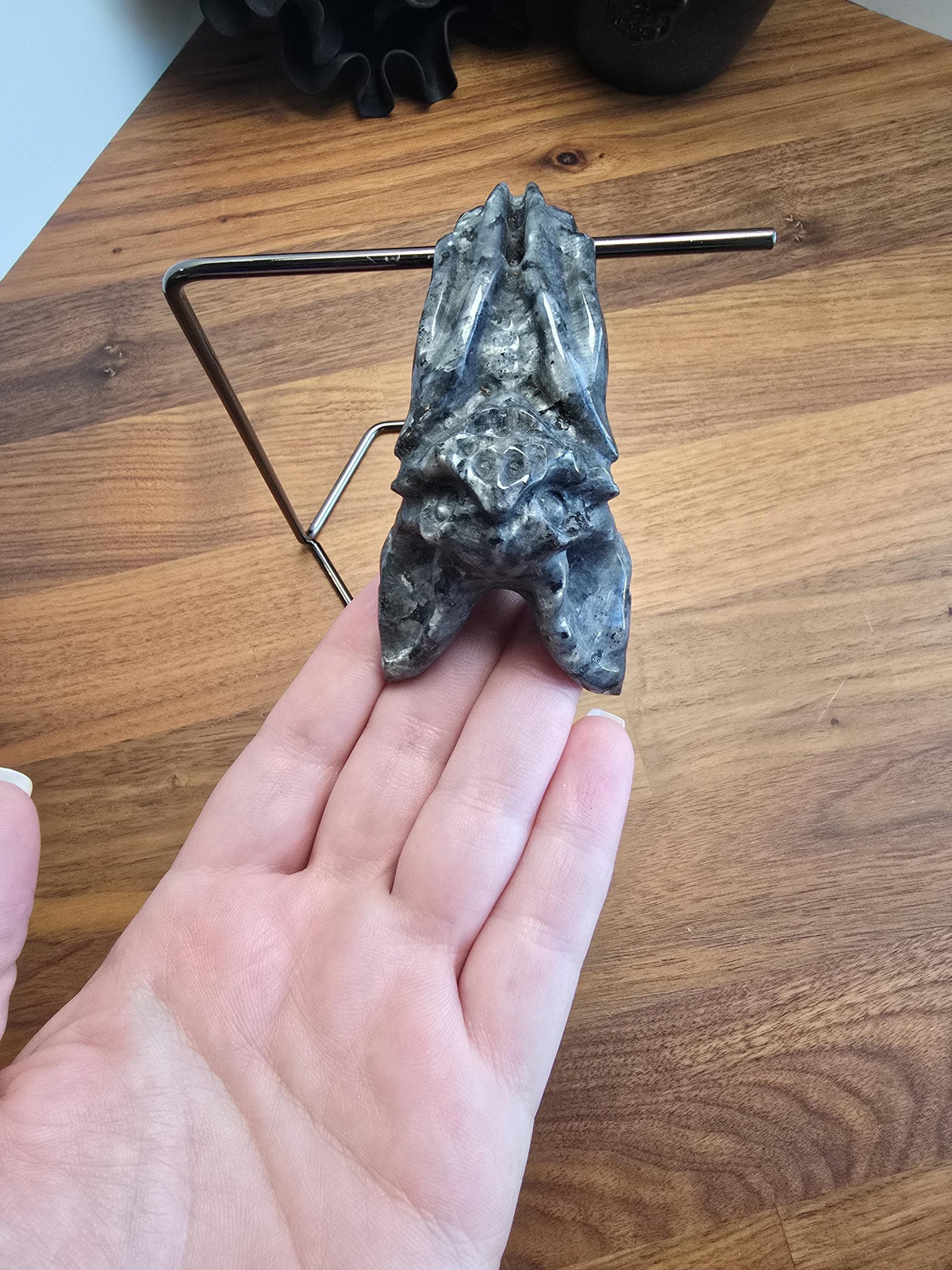 A hand is holding a small, gray stone bat sculpture on a wooden surface.