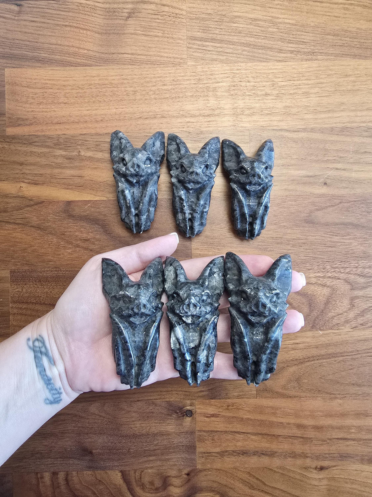 A hand holding five dark gray bat-shaped objects against a wooden background.