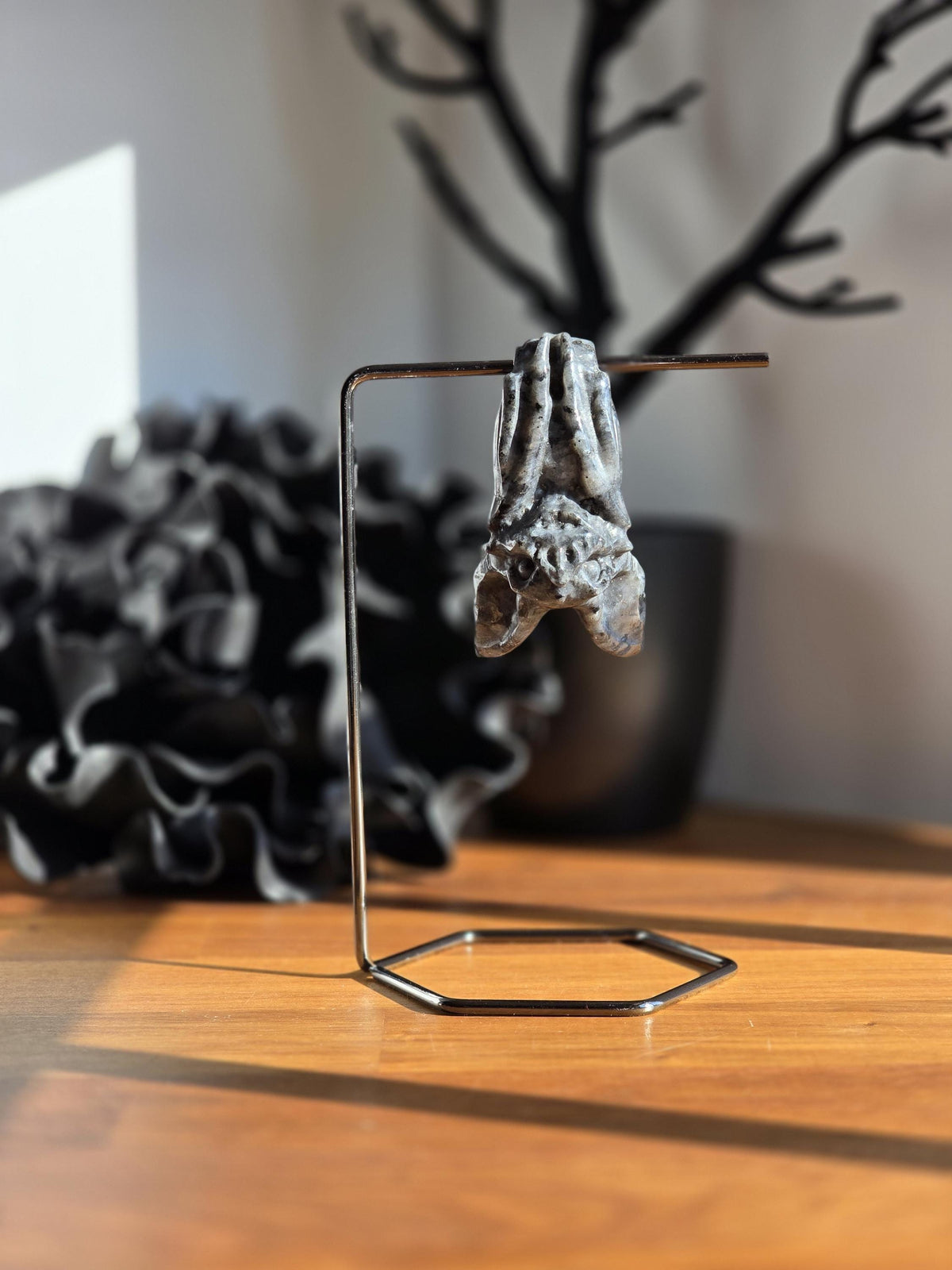 a small sculpture of a bat hanging from a metal stand on a wooden surface.