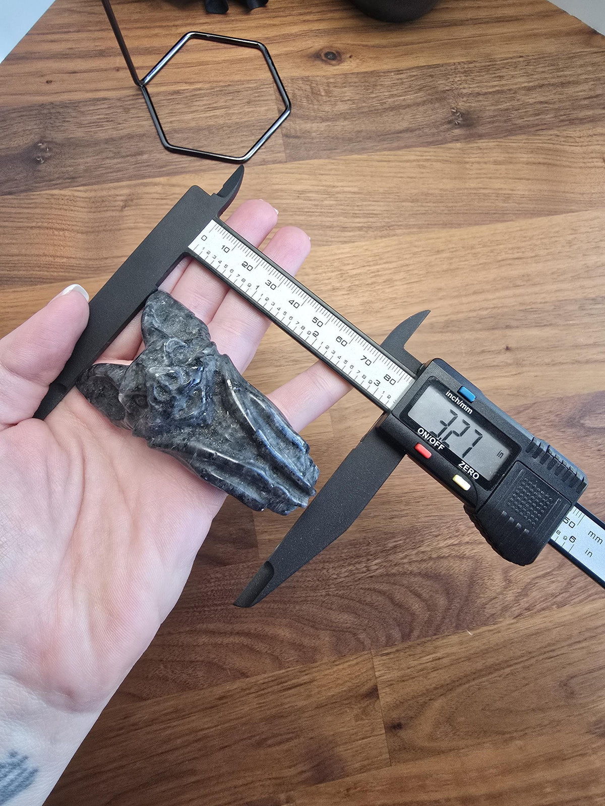 A person's hand holding a small bat-shaped object, with a ruler and a digital caliper placed on top of it.